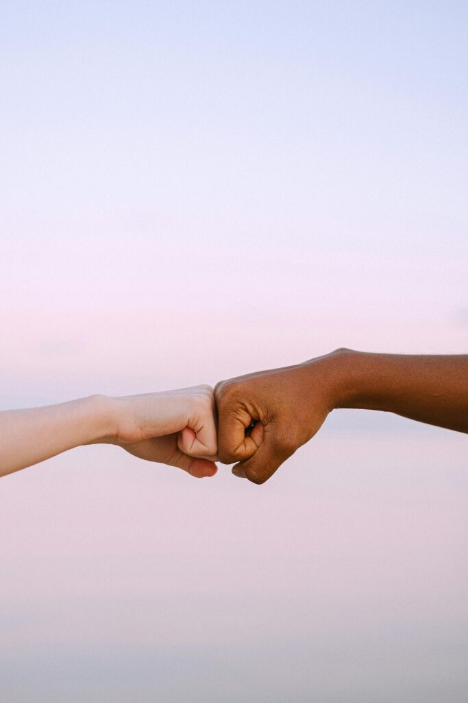 Two diverse hands fist bump against a soft pastel background, symbolizing unity and friendship.